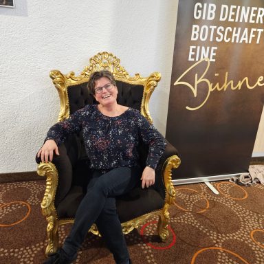 Frau sitzt auf einem goldenen Thron vor einem Banner mit der Aufschrift „Gib deiner Botschaft eine Bühne“.
